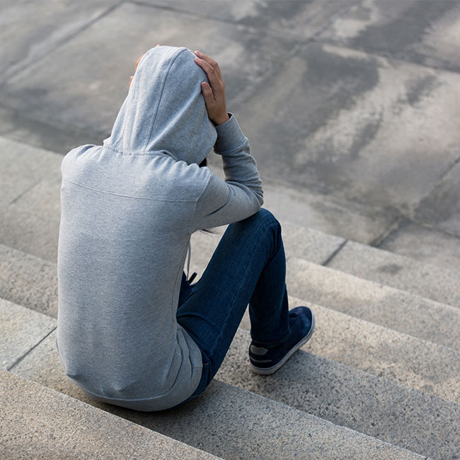 male in a grey hoodie sat on concrete steps with head in hands
