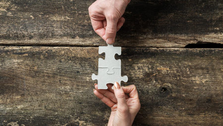 2 jigsaw pieces being fit together by 2 people's hands