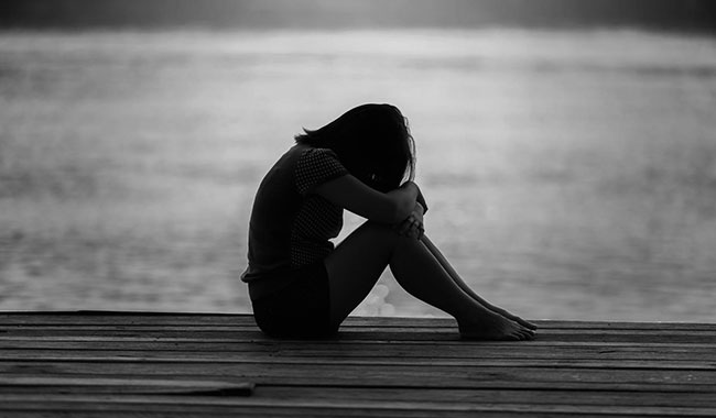 woman sat on decking by water resting head and arms on knees