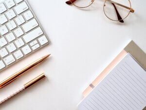 A stylish desk with a keyboard, notebook, pen, and glasses, ideal for making notes about an online resource