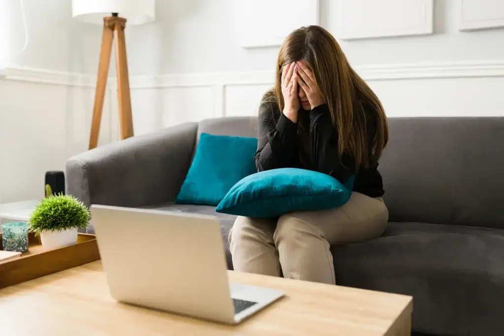 A woman sitting on a couch, hands on her face, during an online therapy session with a human therapist.